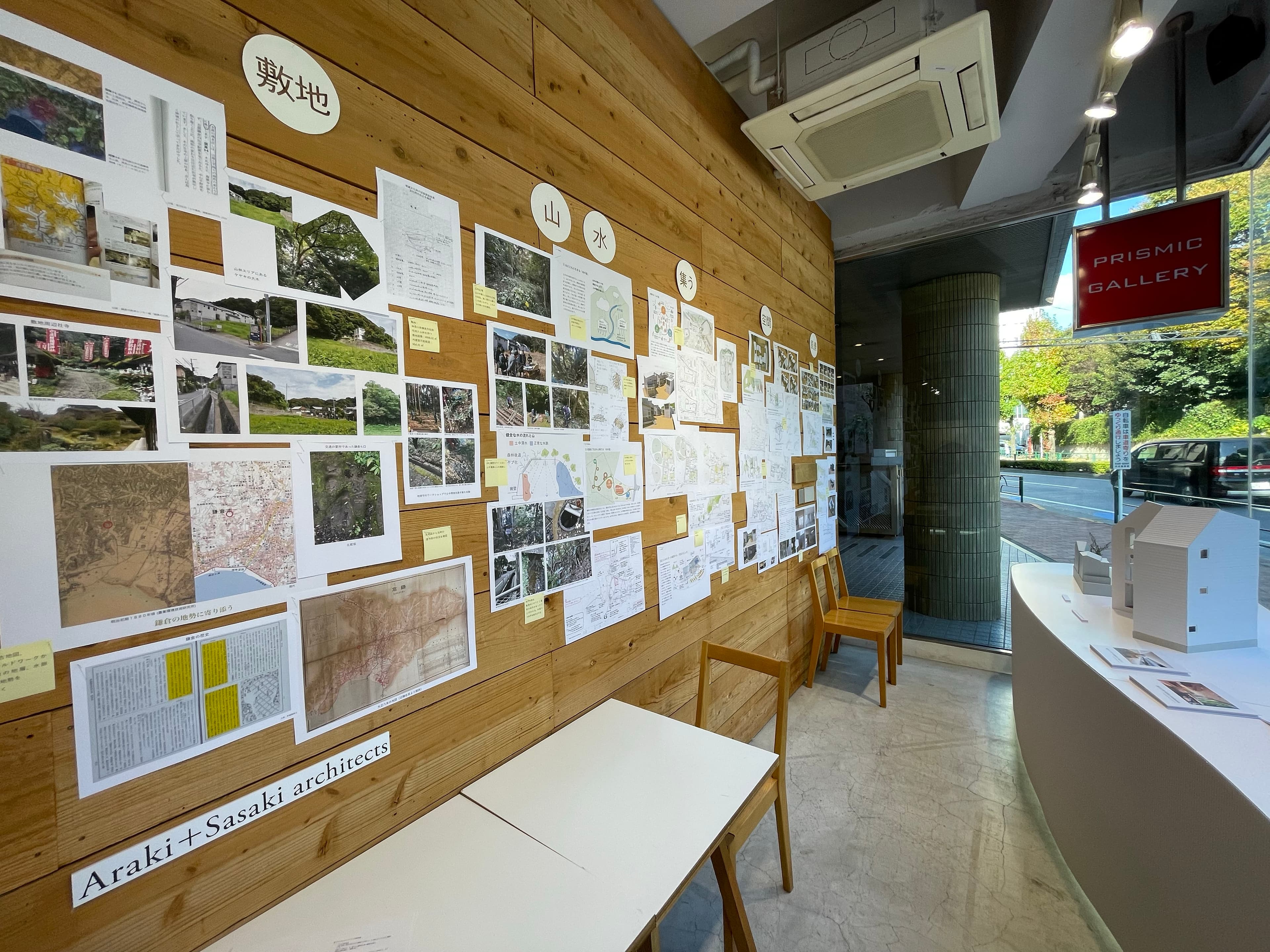 木壁に敷地調査の写真や地図、資料が多数貼られたリサーチ展示。「敷地」「山」「水」「集う」などの見出しとともに、鎌倉の地勢や敷地周辺の写真が並ぶ